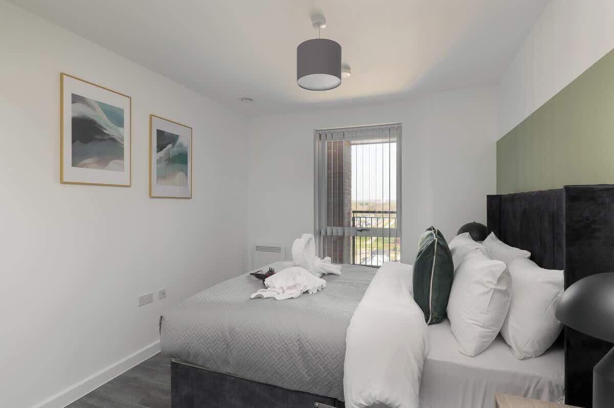 Una habitación de hotel moderna con una cama, un ventanal con cortinas y dos cuadros enmarcados en la pared.