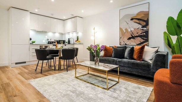 Ein modernes Wohnzimmer mit einem grauen Sofa, einem Couchtisch und einem Essbereich mit Stühlen.