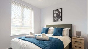 Un dormitorio con cama, mesita de noche, lámpara y ventana con persianas.