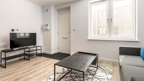 Una sala de estar moderna con un televisor de pantalla plana sobre un mueble negro, un sofá gris y una alfombra estampada.
