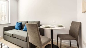 Una sala moderna con un sofá gris, dos sillones y una mesita redonda con un plato blanco y un vaso.