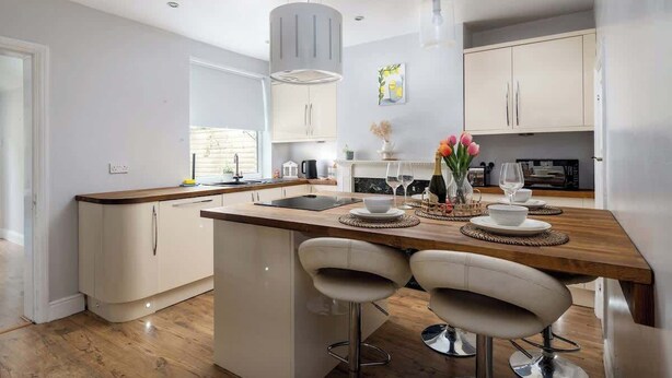 A modern kitchen with a central island, white cabinetry, and a dining area with two bar stools. - Better Than a Hotel | Parking | Stony Stratford (Milton Keynes)