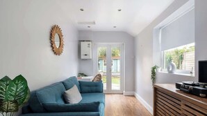 A modern living room with a teal sofa, a wooden cabinet with a record player, and a large window. - Better Than a Hotel | Parking | Stony Stratford (Milton Keynes)