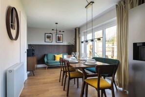 Uma área de refeições com uma mesa de madeira posta para quatro pessoas, um sofá verde e um radiador.
