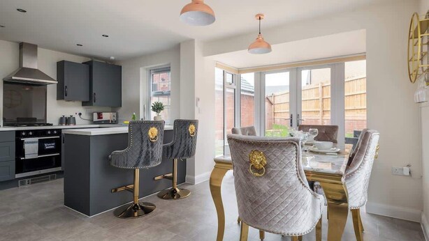 A modern kitchen with dark cabinetry, a central island, and pendant lighting. - 4 Bedroom Detached House (Milton Keynes)