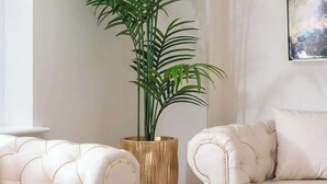A modern living room with a white sofa, a large potted plant, and a chandelier. - 4 Bedroom Detached House (Milton Keynes)