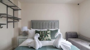 A neatly made bed with two swans made of towels, a grey headboard, a green pillow, and a grey bench beside the bed. - 4 Bedroom Detached House (Milton Keynes)