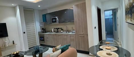 A modern living room with a sofa, a glass dining table, and a kitchen in the background.