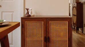 A room with a wooden cabinet with a woven front panel, a white door, and two wall-mounted planters with greenery. - NEW - Stylish Art Deco Apt • Easy Access to Manhattan (Hoboken)