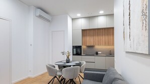 A modern kitchen with wooden cabinets, a dining area with a round table and grey chairs, and a grey sofa in a living area. - Vytauto 43 Residence – Lietūkis by Domvia (Kaunas)