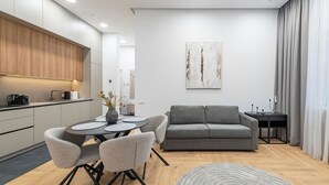 A modern living room with a grey sofa, a dining table with chairs, and a kitchen area with wooden cabinets. - Vytauto 43 Residence – Lietūkis by Domvia (Kaunas)