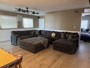 A living room with a sectional sofa, a wooden floor, and a ceiling fan. - Hit the Trail or Lake: Spacious 4BR/2BA Retreat with Pool Table & Large Bar Area (Needles)