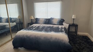 A bedroom with a large bed, two bedside tables with lamps, a mirror, and a window with blinds. - Hit the Trail or Lake: Spacious 4BR/2BA Retreat with Pool Table & Large Bar Area (Needles)