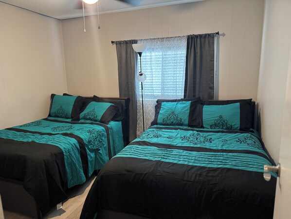 A room with two single beds, each with teal and black bedding, a ceiling fan, and a window with patterned curtains. - Hit the Trail or Lake: Spacious 4BR/2BA Retreat with Pool Table & Large Bar Area (Needles)
