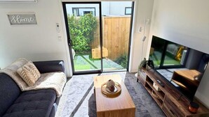 A modern living room with a dark sofa, a wooden coffee table, and a TV on a wooden stand. - Central 2BR Townhouse with Private Yard (Christchurch)