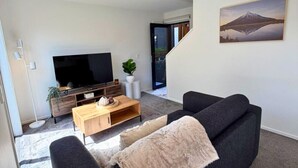 A modern living room with a black sofa, a wooden coffee table, and a flat-screen TV on a wooden stand. - Central 2BR Townhouse with Private Yard (Christchurch)