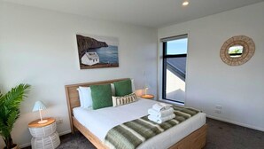 A modern bedroom with a large bed, a potted plant, a bedside table, and a window with a view. - Central 2BR Townhouse with Private Yard (Christchurch)