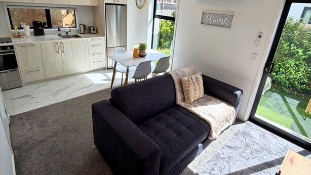 A modern living room with a sofa, a dining table, and a kitchen area with cabinets and a refrigerator. - Central 2BR Townhouse with Private Yard (Christchurch)