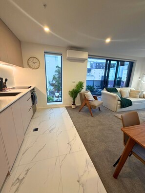 Eine moderne Wohnung mit Küche, Essbereich und Wohnzimmer. Sie verfügt über ein großes Fenster, eine Uhr und eine Klimaanlage.