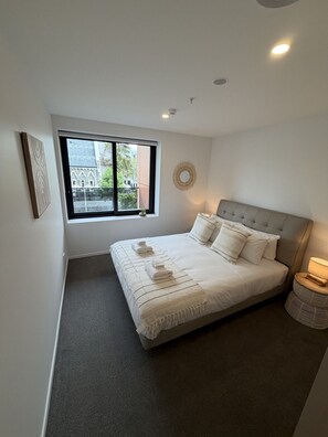 Een slaapkamer met een groot raam, een bed met witte lakens, een ronde wanddecoratie en een bedlamp.