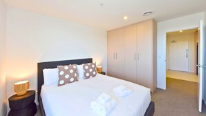 Una camera d'albergo con un letto, una lampada da comodino, un armadio e una porta aperta che dà su un'altra stanza.