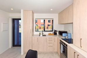 A modern kitchen with light wood cabinets, a built-in oven, and a window overlooking a red building. - Stylish 2BR Townhouse with Balcony (Christchurch)