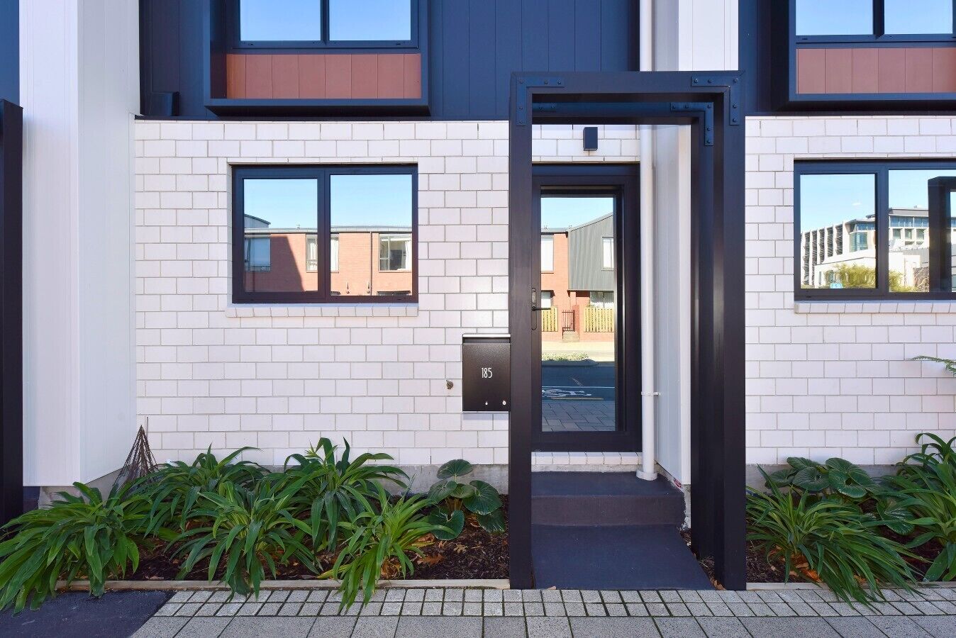 A modern building with a white brick exterior, a black-framed door, and a visible mailbox.