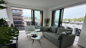 Ein modernes Wohnzimmer mit einem grauen Sofa, zwei weißen Sesseln, einem kleinen runden Tisch und einem großen Fenster mit Blick auf die Stadt.