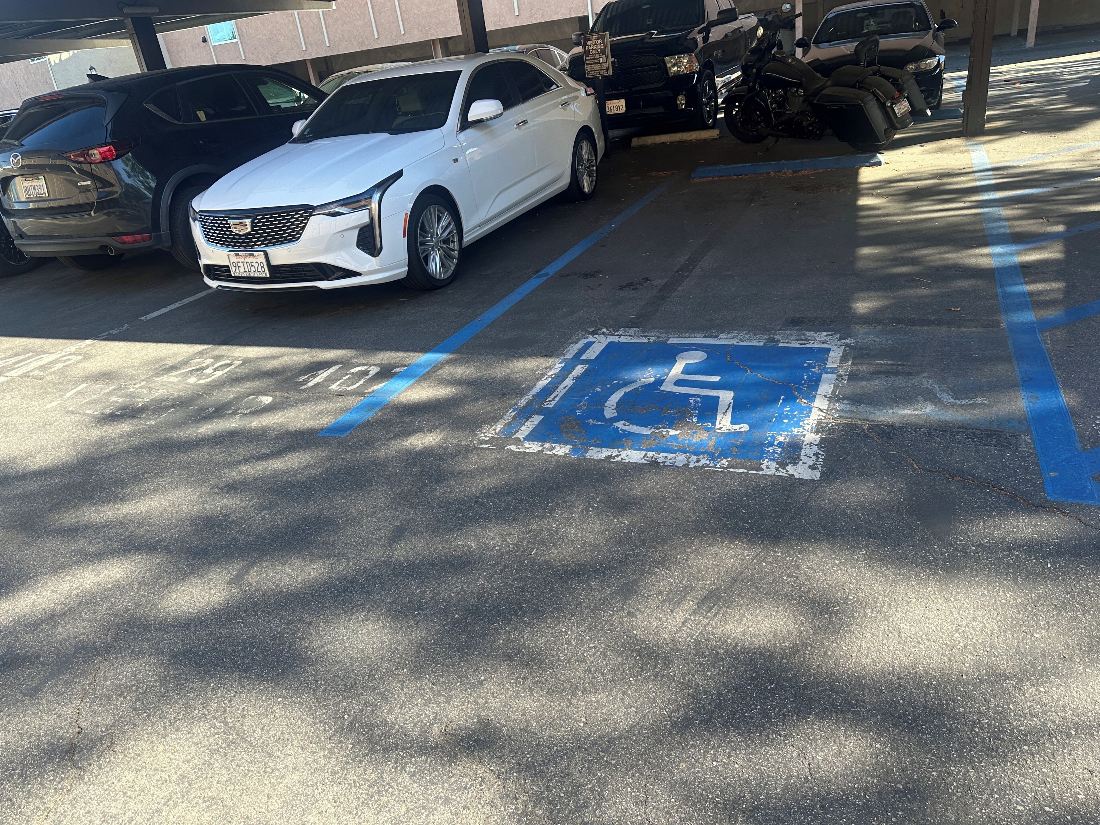 A parking space marked with a wheelchair accessibility symbol, a white car parked, and a motorcycle in the background.