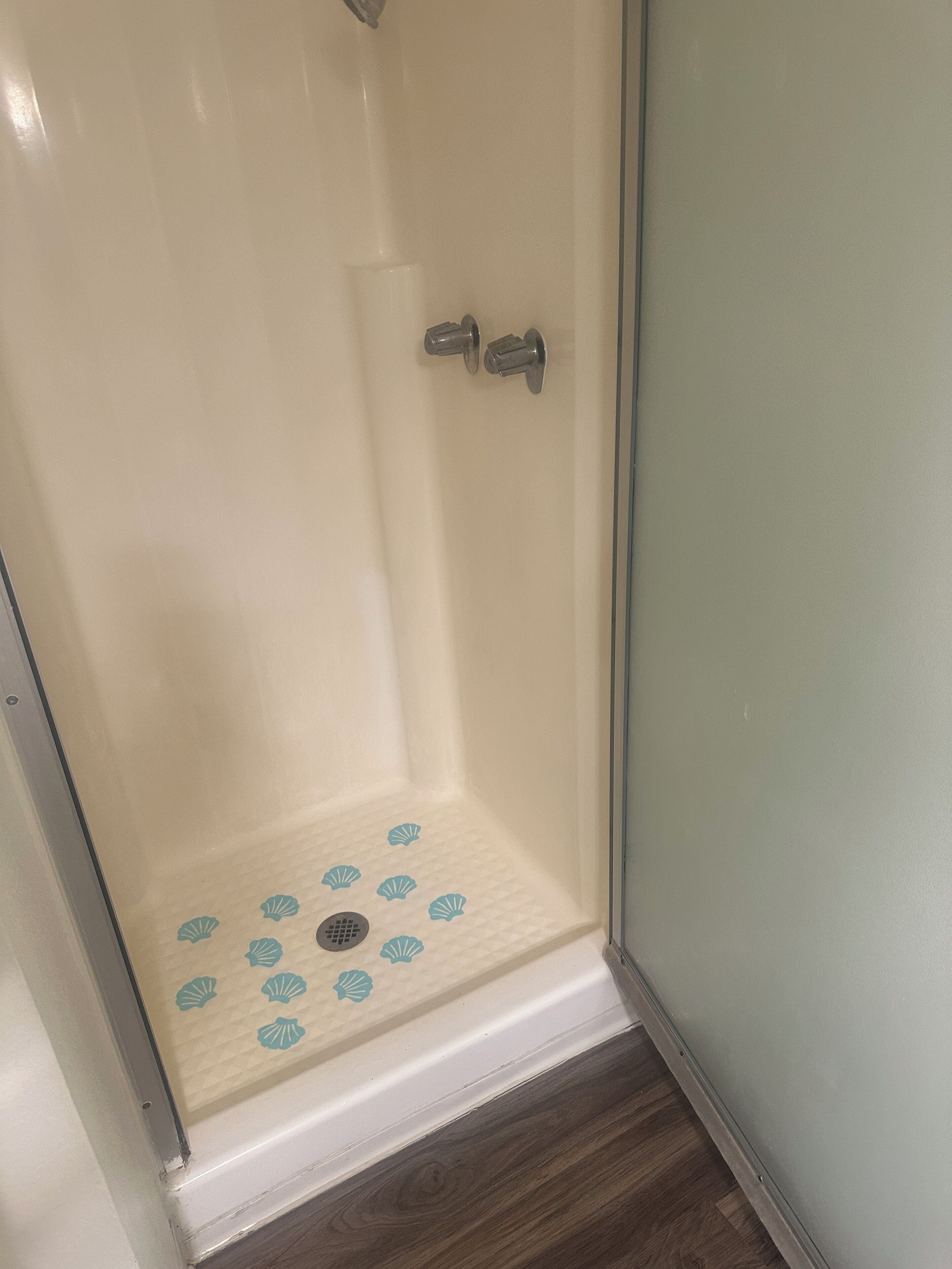 A glass-enclosed shower with a tiled floor and a drain.