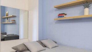 Ein Schlafzimmer mit einem Bett, Kissen, einem Spiegel und zwei Regalen mit Büchern und einer Vase.