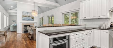 A modern kitchen with white cabinetry, a central island, stainless steel appliances, and a dining area with a view of the outdoors.
