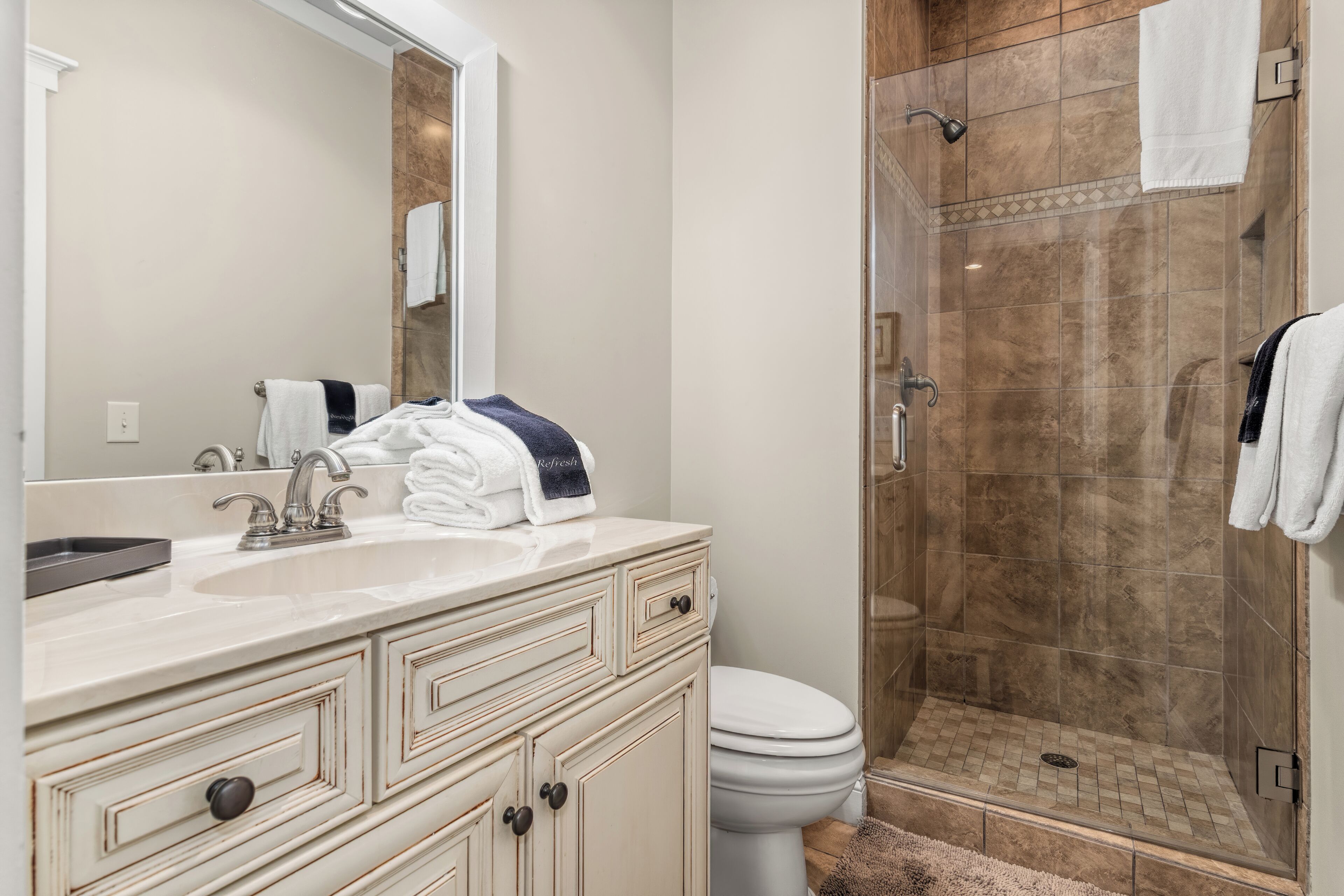 A bathroom with a sink, mirror, towel rack, and a shower area.