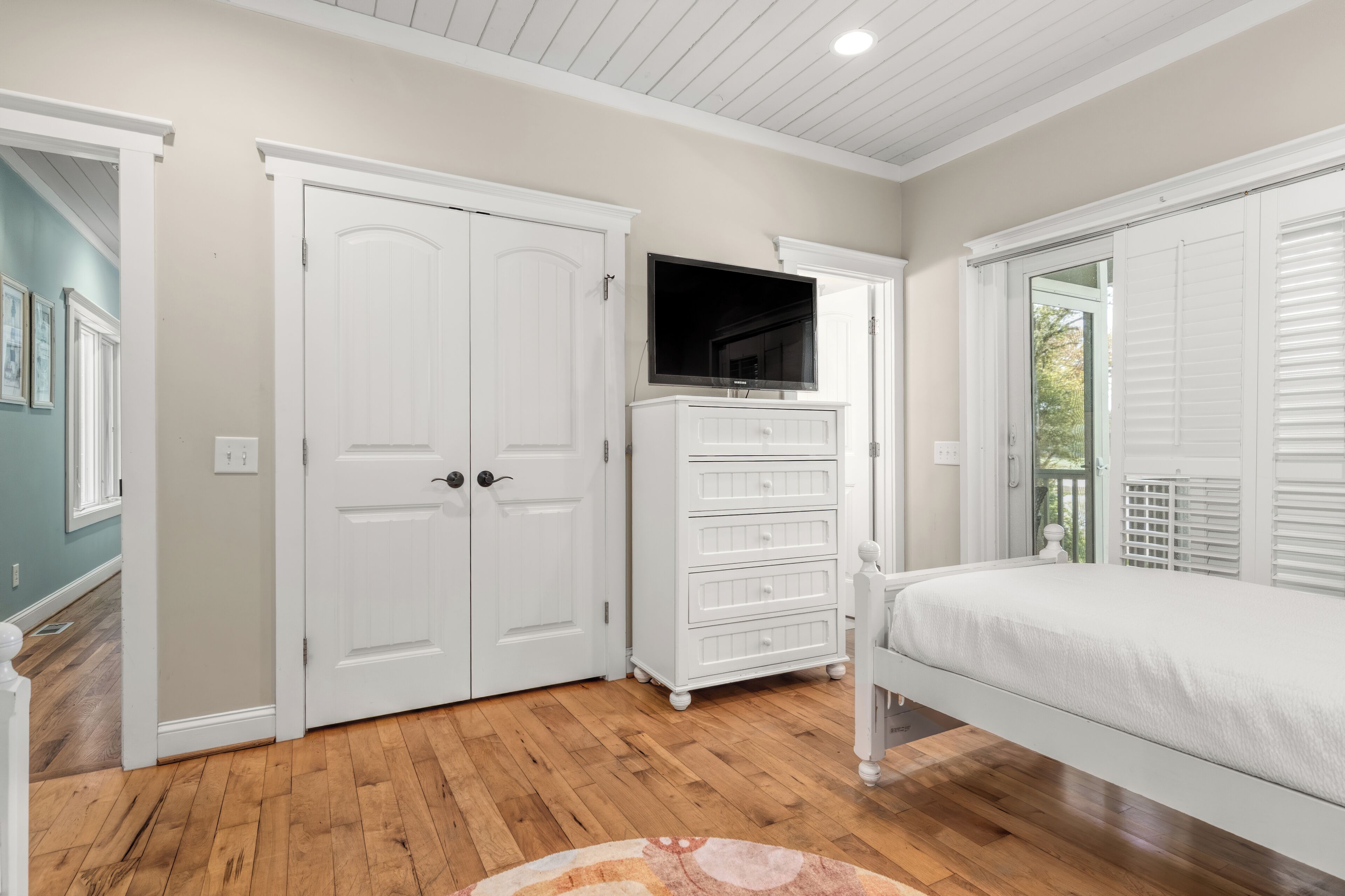 A bedroom with a bed, a dresser, a television, and a door.