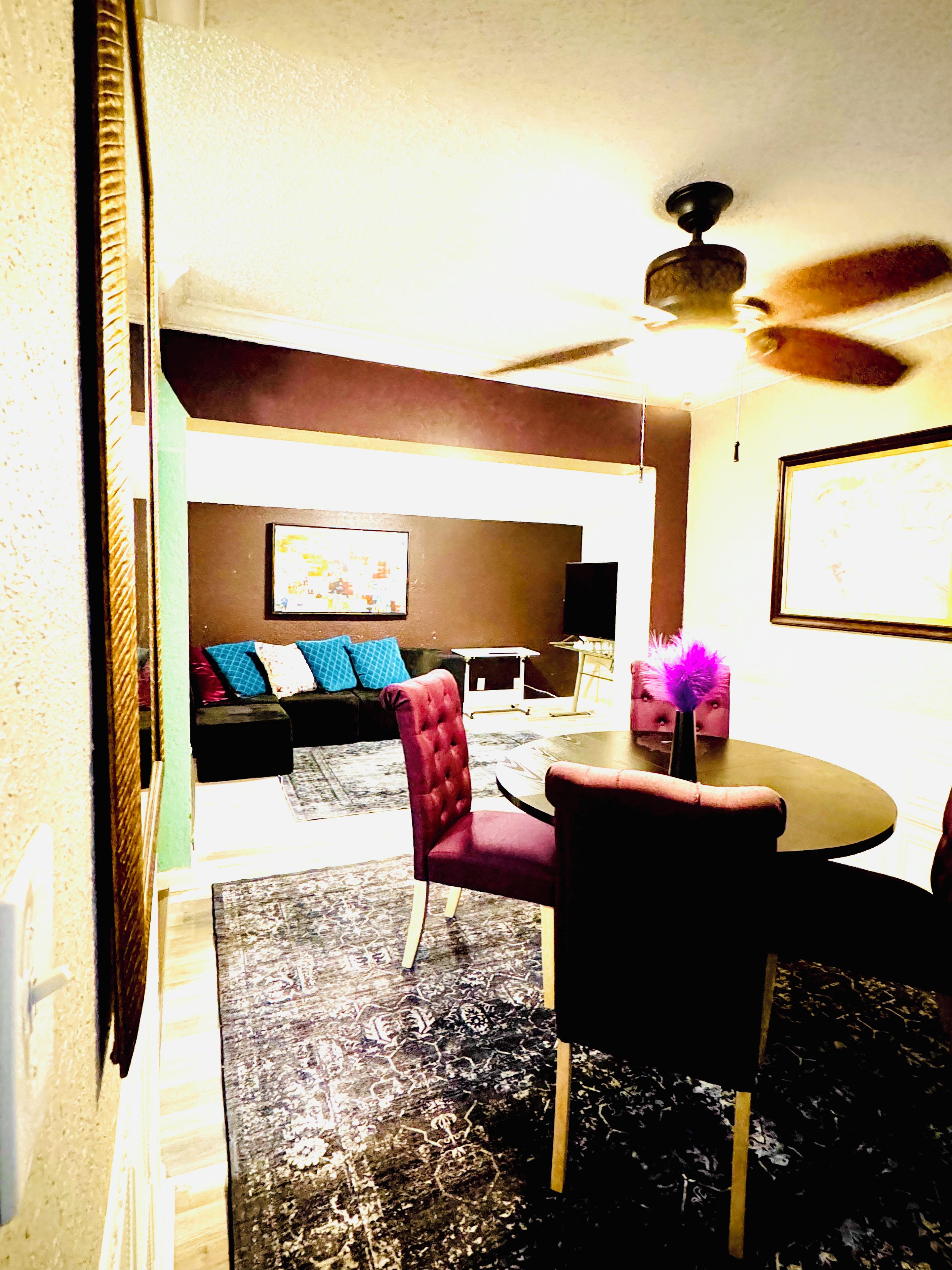 A dining area with a round table, chairs, a ceiling fan, and a sofa with cushions.