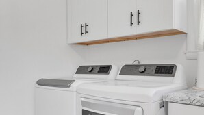 A laundry area with two washing machines and a dryer, wooden bench, white cabinets, and a marble countertop. - 5Min to Downtown Franklin/Pet Friendly/Fenced Yard (Franklin)