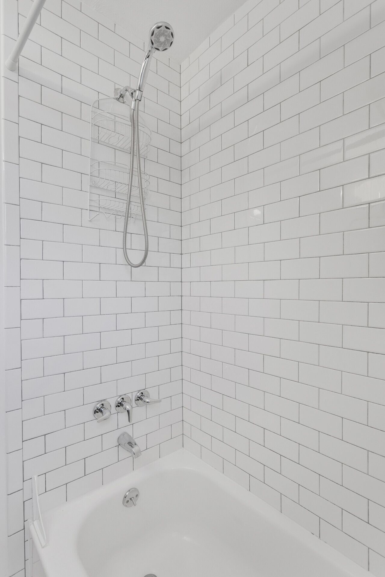 A bathroom with white subway tiles, a shower with a handheld showerhead, and a bathtub with two faucets.
