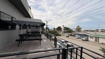 A balcony with a picnic table and a view of a street with parked cars and buildings.