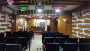 Un salón de conferencias con filas de sillas, un escenario con un atril y globos decorativos.