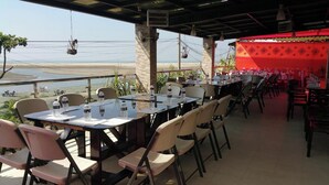 Un área de comedor al aire libre con mesas y sillas, con vista a una playa.