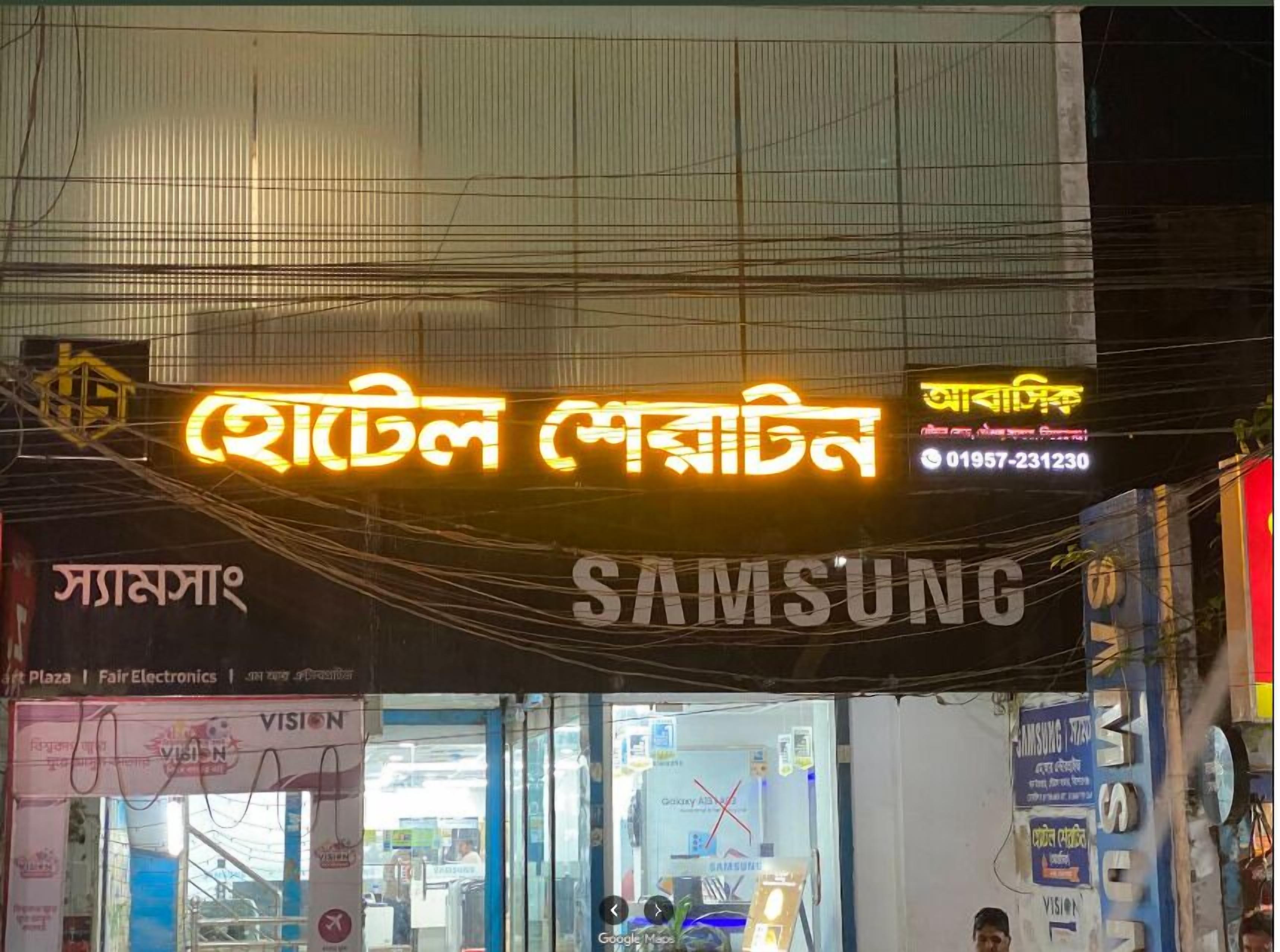 Una vetrina con un neon in caratteri di una lingua straniera, un cartello Samsung e un ingresso con porta in vetro.