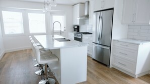 Une cuisine moderne avec des meubles blancs, un réfrigérateur en acier inoxydable, une cuisinière à gaz et un coin bar avec des tabourets.