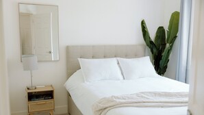 Une chambre à coucher avec un lit, une table de chevet, une lampe et une grande plante.