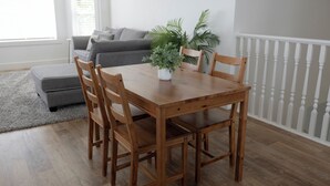 Un coin repas avec une table et des chaises en bois, un canapé gris, une rambarde blanche et une plante en pot.