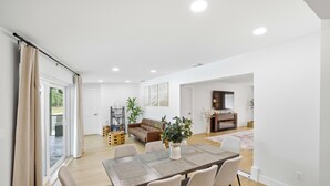 Ein geräumiger Wohnbereich mit Esstisch, Stühlen, einer Couch und einem Couchtisch. Eine Glastür öffnet sich zu einem Balkon.