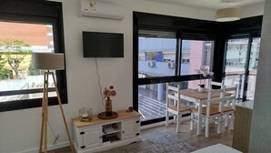 Un dormitorio moderno con un ventanal grande, un televisor de pantalla plana, una mesita de noche con lámpara y vistas a la ciudad.
