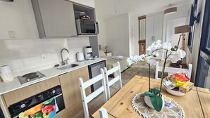 Una cocina moderna con horno integrado, microondas y cafetera. Hay una mesa de comedor con sillas y una planta decorativa.