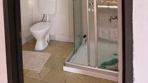 Un bagno con cabina doccia in vetro, un water e pavimento in piastrelle bianche.