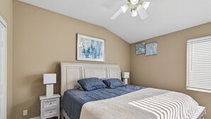 Um quarto com cama, mesas de cabeceira, ventilador de teto e obras de arte nas paredes.
