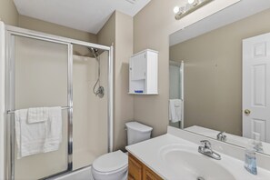 Une salle de bain avec une douche à parois de verre, des toilettes blanches, un lavabo avec un miroir et un meuble au-dessus des toilettes.